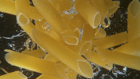 Falling uncooked italian pasta Penne into water.の写真素材