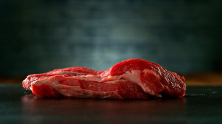 Flying pieces of raw beef steak on stone table, grey brick wall on background.