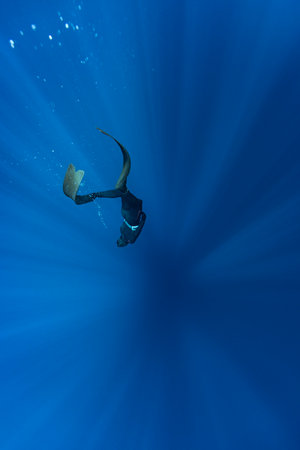 Freediver Swimming in Deep Sea With Sunrays. Young Man DIver Eploring Sea Life.
