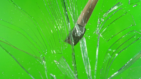 Freeze motion of glass-breaking hammer, shattering against green background