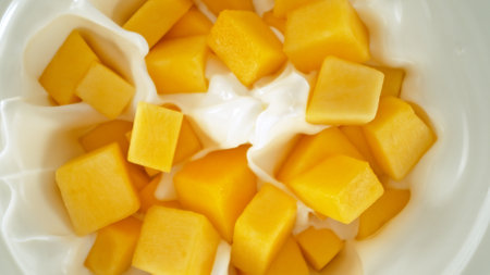 Fresh mango pieces falling into yoghurt cream, top down viewの写真素材