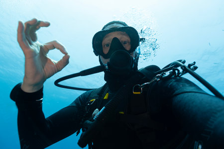 Scuba diver man swimming on a blue water sea looking at cameraの写真素材