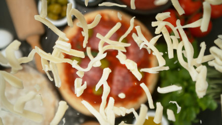 Super slow motion of falling fresh basil leaves on pizza dough with sugo, top down view