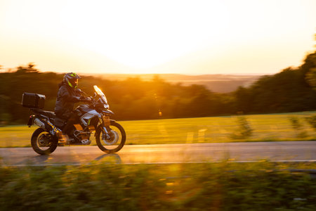 Driver riding motorcycle on empty road during sunset, spring mountainsの写真素材