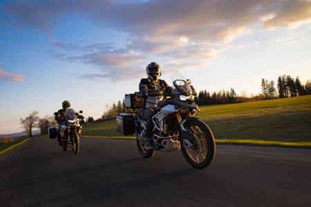 Drivers riding motorcycle on empty road during sunset, spring mountainsの写真素材