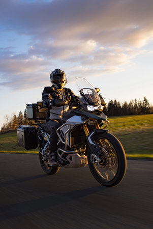 Driver riding motorcycle on empty road during sunset, spring mountainsの写真素材