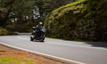 Driver riding motorcycle on empty asphalt road, spring mountainsの写真素材