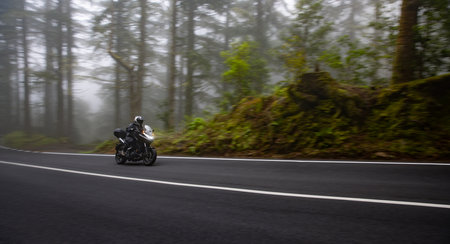 Driver riding motorcycle on empty road , foggy rainforest, spring mountains