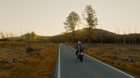 Driver riding motorcycle on empty asphalt road, spring mountains during sunsetの写真素材