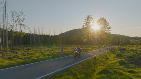 Driver riding motorcycle on empty asphalt road, spring mountains during sunsetの写真素材