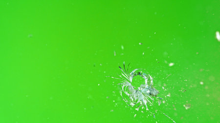Close-up of gunshot through the glass, shattering against the green background