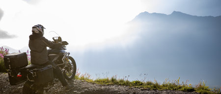Motorcycle rider in Italian Alps during sunrise, dramatic sky. Travel and freedom, outdoor...