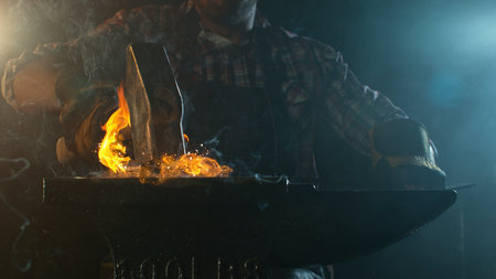 Close-up of blacksmith forging glowing hot iron on anvil with flying sparksの写真素材