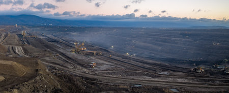 Aerial view of an active coal mining site showcases heavy machinery and smoke billowing into the air