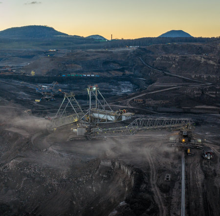Aerial view of an active coal mining site showcases heavy machinery and smoke billowing into the air