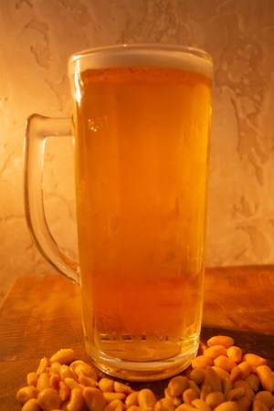 glass of light cold frothy beer, nuts on an old wooden tableの写真素材