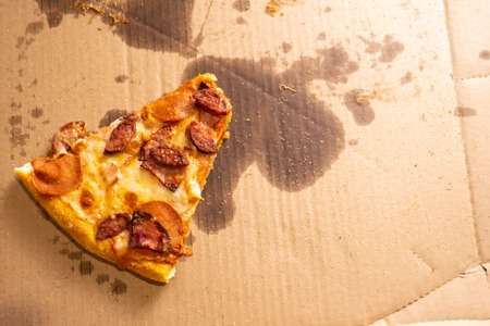 A small slice of pizza remaining in a large cardboard box with oil stains.の写真素材