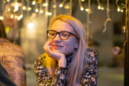 Portrait of young beautiful happy smiling girl in glasses and garland light. christmas portrait.の写真素材
