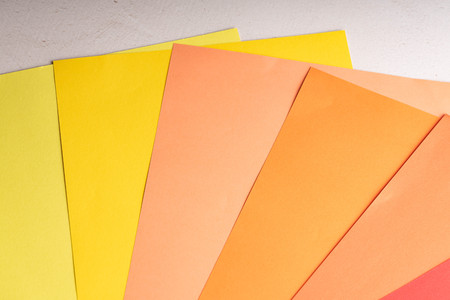 Sheets of colored paper are on the table. Paper of blue, yellow, green, blue, red, coral and peach...