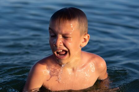 A boy of nine is swimming in the sea at sunsetの写真素材