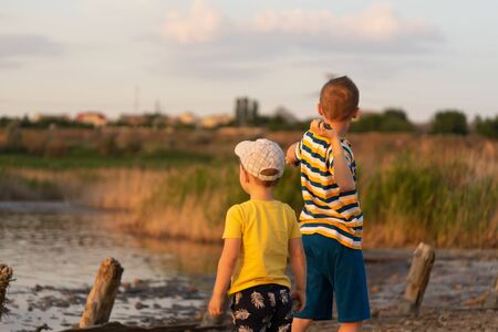 Two brothers, the boys 3 years old and 9 years old, watching the sunset on the lake sun.の写真素材