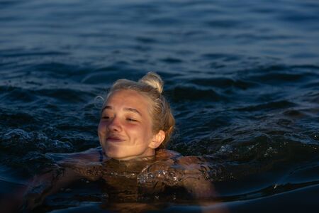 A girl of 17 years old is swimming in the sea and smiling