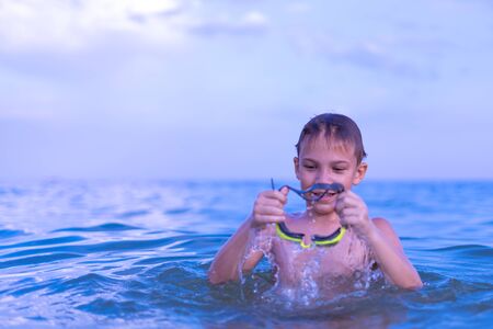 A 10-year-old boy swims in the sea at dawn with glasses for swimmingの写真素材