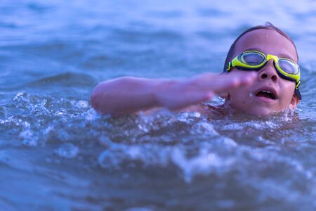 A 10-year-old boy swims in the sea at dawn with glasses for swimmingの写真素材