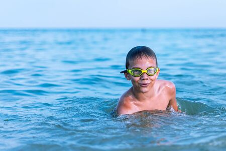 A 10-year-old boy swims in the sea at dawn with glasses for swimmingの写真素材