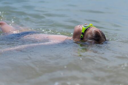 A boy of 10 years old is swimming in the sea on a clear sunny dayの写真素材