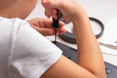 A boy of 10 years old is sorting a laptop for cleaning and maintenance. Selective focus. Screwdrivers, purge cylinder, magnifying glass and spray cleaner in the frame.の写真素材