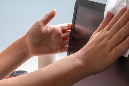 A teenager boy of 10 years old is cleaning his laptop with a special cloth and cleaning agentの写真素材