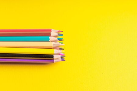 Many sharpened colored pencils laid out on a yellow background. Copyspace
