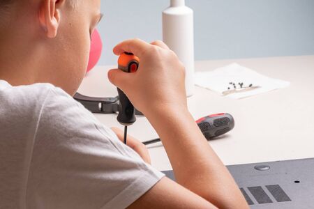 A boy of 10 years old is sorting a laptop for cleaning and maintenance. Selective focus. Screwdrivers, purge cylinder, magnifying glass and spray cleaner in the frameの写真素材