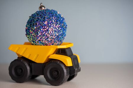 Yellow dump truck model with Christmas tree toy. Garland lights in defocus