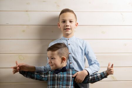 A 4-year-old boy in a blue klepy shirt cries on a light wooden background and his brother, 10 years old, is standingの写真素材