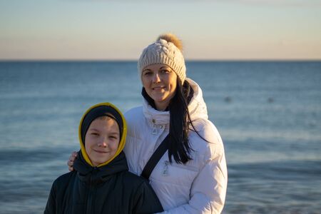 A woman with her son in ordinary clothes while walking on the seashore on a sunny winter dayの写真素材
