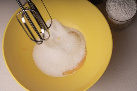 A woman mixes the ingredients for a pie in a yellow bowl with an electric mixerの写真素材