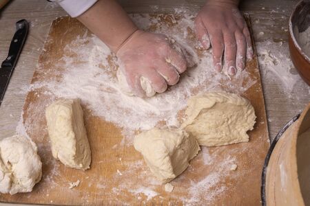A woman kneads the dough. Plywood cutting board, wooden flour sieve and wooden rolling pin - tools...