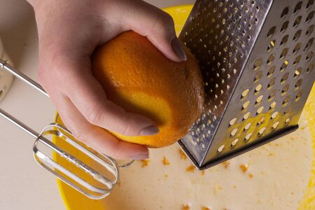 Female hands rubbing the zest of an orange on a metal graterの写真素材