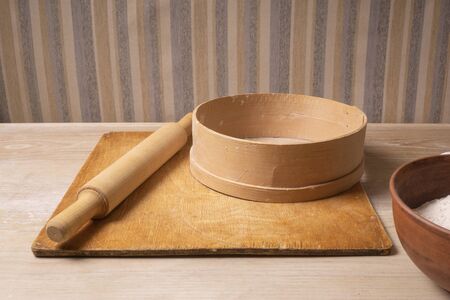 Plywood cutting board, wooden flour sieve and wooden rolling pin - tools for making dough.
