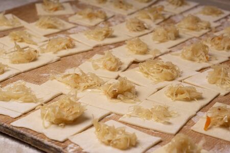 A rectangular piece of dough with cabbage - for making ravioli dumplings. Plywood cutting board, wooden flour sieve and wooden rolling pin - tools for making dough.の写真素材