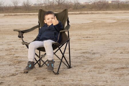 A 4-year-old boy sits on a folding chair on an empty beach during quarantine.