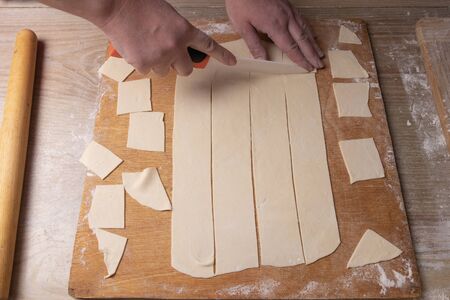 Female hands slices the dough on a cutting board with a white knife. Cooking at home
