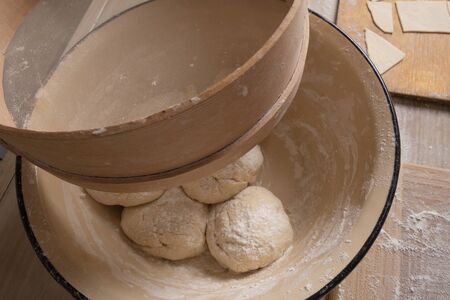 Balls of dough are in a large yellow bowl. Cooking at home