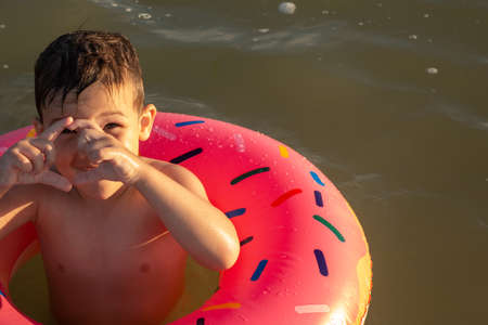 A 5-year-old boy swims in the sea with a donut-shaped inflatable circle and tells what a big jellyfish he just saw in the seaの写真素材