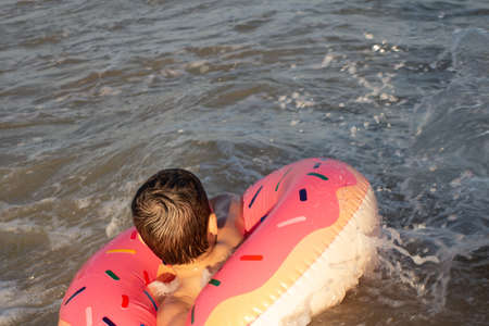 A cheerful boy 5 years old swims in the sea on an inflatable ring in the form of a donut on a sunny...