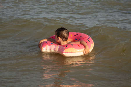 A cheerful boy 5 years old swims in the sea on an inflatable ring in the form of a donut on a sunny...
