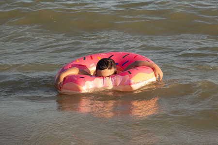 A cheerful boy 5 years old swims in the sea on an inflatable ring in the form of a donut on a sunny...