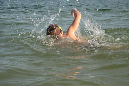 Young swimmer in goggles swims to crawl in the open sea